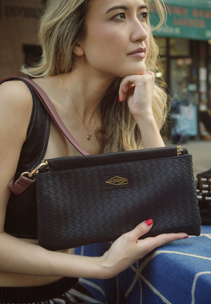 Woman holding a black handbag with a visible brand logo in an urban setting