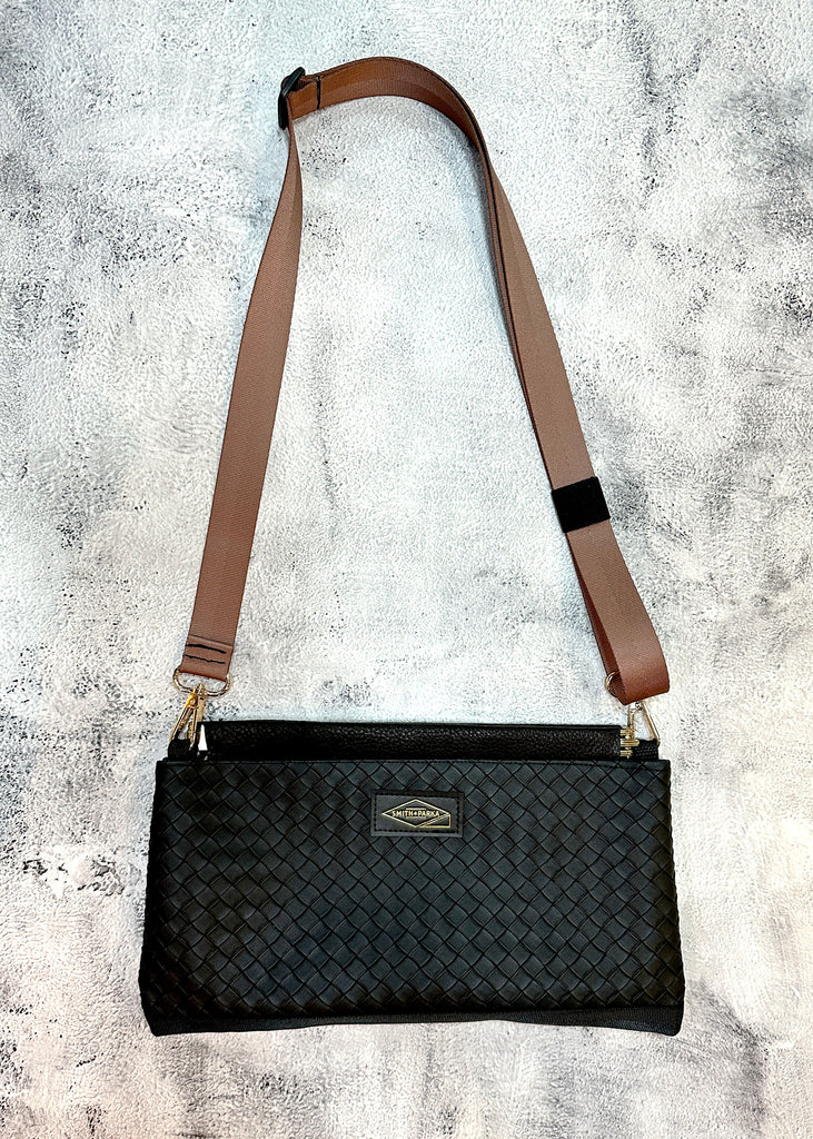 Black woven handbag with a brown strap on a textured gray background