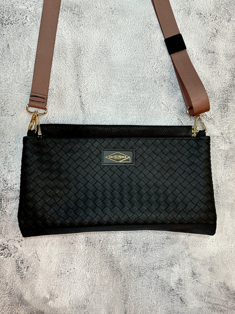 Black woven handbag with a brown strap on a textured gray surface