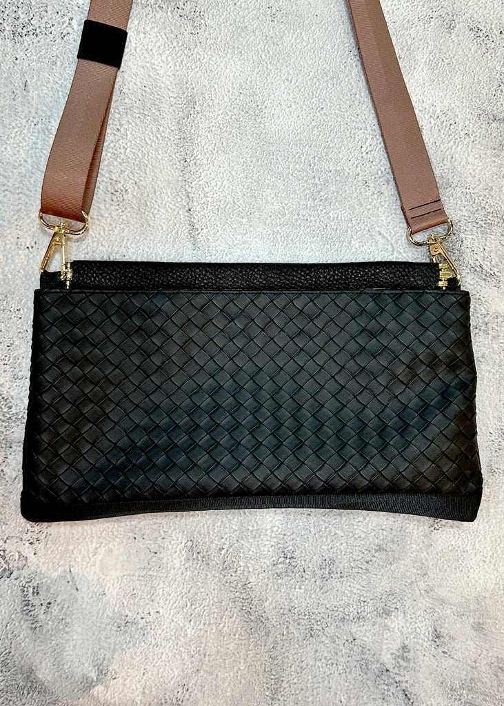Black woven handbag with a brown strap on a gray surface